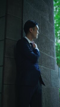 Japanese businessman pausing to think in the shade of an office building