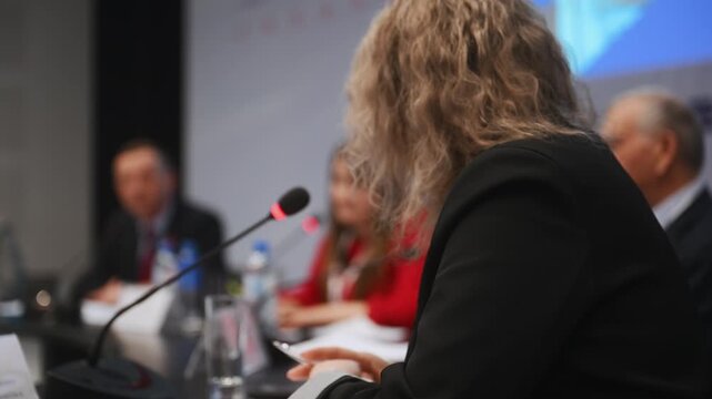 Conference speaker using a microphone during a professional panel discussion with participants. Business communication, public speaking, corporate event and expert meeting concept.