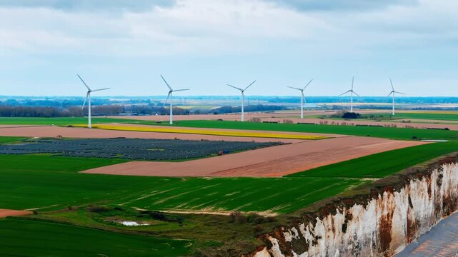 Wind turbines on farmland and solar panels near Normandy coast, France. Clean energy infrastructure beside English Channel landscape