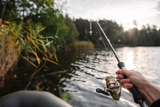 Angler fishing with a spinning rod from an inflatable boat near the reeds on a calm lake, catching fish during a sunny afternoon outdoors.