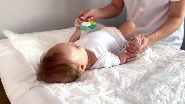 Mother gives teether toy to infant baby,developing pincer grasp, focused attention.Physical therapist exercising newborn little child,motherhood,baby care,wellness