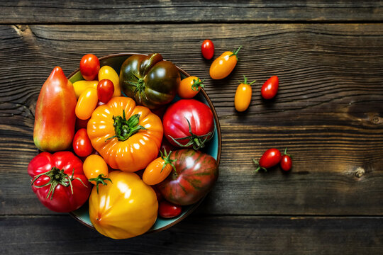 Top view of assorted fresh heirloom tomatoes in a bowl and scattered on a rustic wooden table.