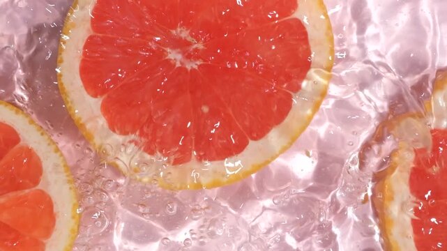 Slow motion shot of fresh grapefruit slices dropping into clean water with splash