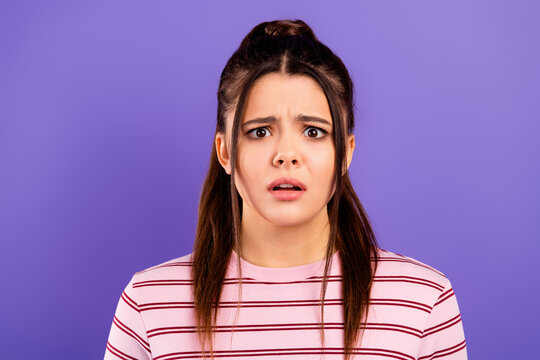 Surprised young woman with raised eyebrows and open mouth looking confused against a purple studio background