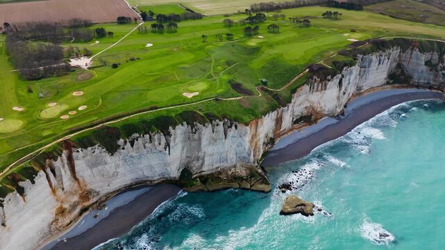 White chalk cliffs beside turquoise sea at Etretat, Normandy, France. Aerial footage of coastal landmark with pebble beaches below steep rock faces.