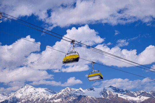 Yellow chairlift seats against the backdrop of a blue sky and surrounding mountains. Sochi.