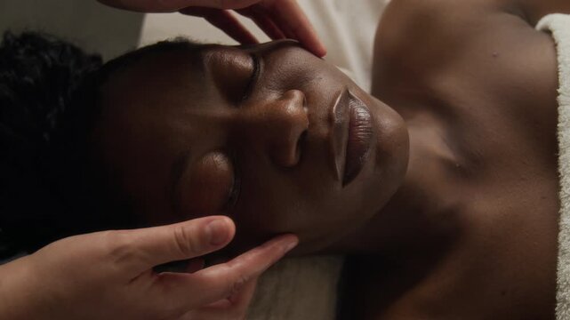 African American young adult woman relaxing while receiving facial massage in luxury spa. Footage suitable for promoting skincare treatments, beauty wellness campaigns and salon advertising