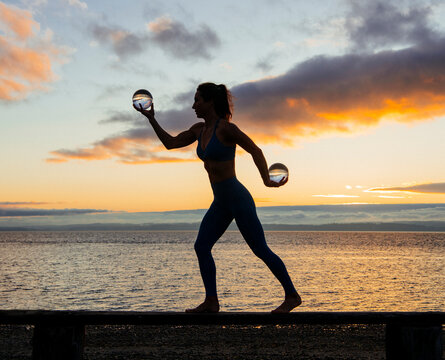 White woman holding glass spheres balancing on pier