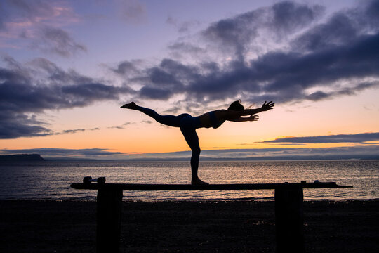 White woman practicing yoga balance pose on beach at sunset