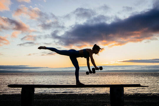 White woman balancing and exercising with dumbbells on a beam at beach