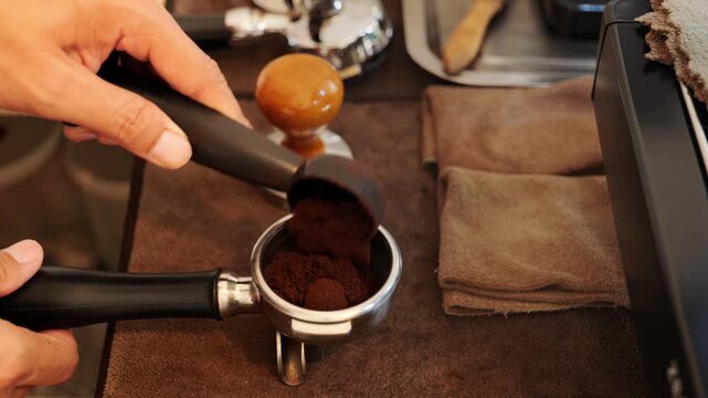 Close-up of hand barista  freshly ground coffee being poured into an coffee portafilter, preparing for extraction.	