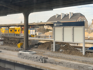 A modern train station information board stands on a dusty platform during reconstruction, conveying urban infrastructure development and travel service disruption in a transit zone © Alina