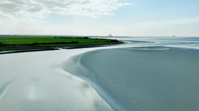 Aerial drone view of broad Normandy bay landscape shaped by tide, with pale sand flats, reflective water and soft coastal patterns