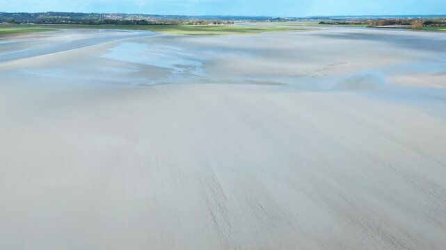 Aerial view over exposed coastal flats in Normandy with broad sandbanks and shallow tidal water shaping the landscape