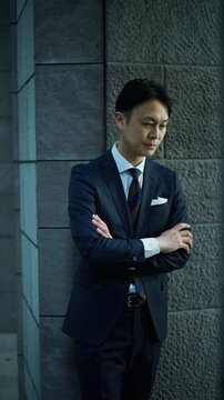 Japanese businessman leaning on a wall with arms crossed and thinking