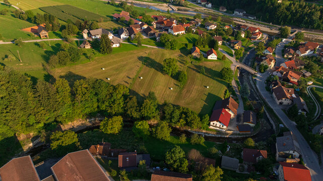 High angle drone shot of Ljubno ob Savinji, Slovenia. Scenic alpine village, Savinja river valley, green agricultural fields, traditional houses with red roofs, church.