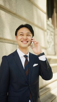 Japanese businessman talking cheerfully on a smartphone outdoors