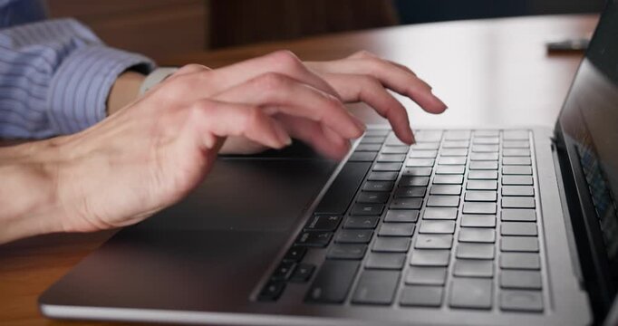 Woman working remotely at table, close-up of hands typing on laptop keyboard.