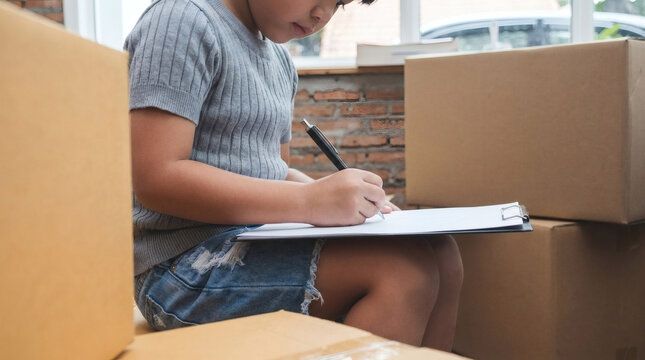 Boy Writing on a Clipboard Amid Moving Boxes