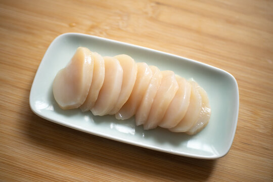 Neatly arranged raw scallop slices on a white ceramic plate against a wooden background.