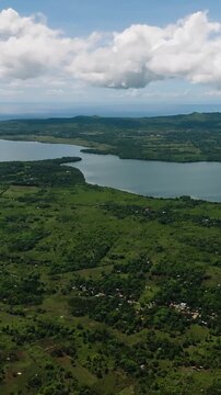 Large freshwater lake surrounded by lush green fields and distant mountains under cloudy blue sky. Camotes, Philippines.