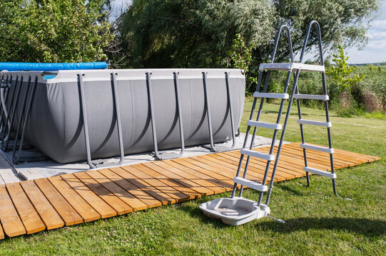 Frame pool with metal ladder stands beside wooden deck on green lawn, representing summer recreation, backyard leisure, home improvement, outdoor living and private pool lifestyle.