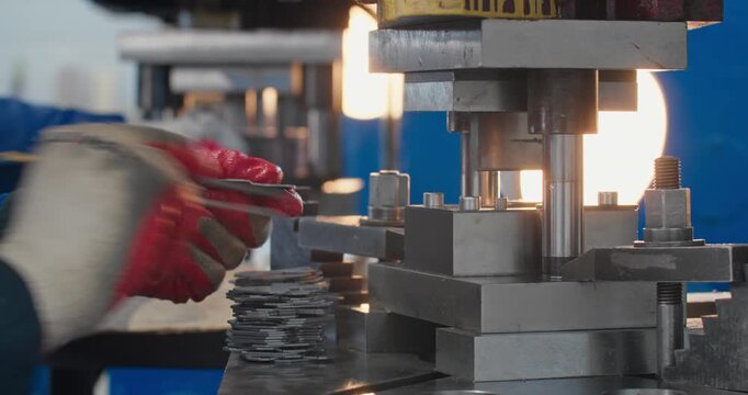 Metal component production on mechanical stamping press, with blue collar worker handling workpiece using tongs