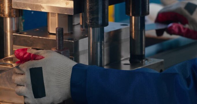 Industrial worker producing metal parts with stamping press. Close-up of blue collar labor and machine operation in metalworking workshop