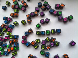 Word ORDER spelled with letter cubes among scattered random alphabet beads background, conceptual flat lay