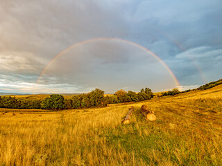 Obraz premium Faint Rainbow Beneath Dramatic Storm Clouds After Rain at Sunrise