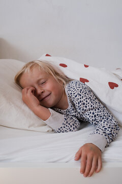  little girl rubbing eyes waking up in cozy bed under duvet with red hearts