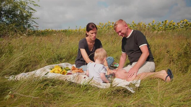 Mother and father spending time with their toddler at a countryside picnic. Family relaxing together outdoors on a sunny day