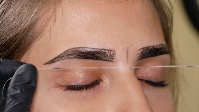 Eyebrow mapping using measuring thread, specialist defining woman's brow shape and symmetry before microblading procedure. Precise preparation for permanent makeup treatment