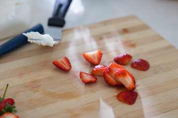 Fototapeta premium Sliced strawberries are glistening on bamboo cutting board near blue-handled utensil, copy space