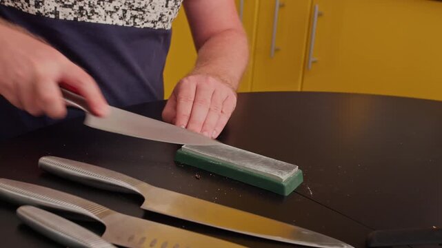 Man maintaining kitchen knives with sharpening stone. Close-up of hands during everyday household chores