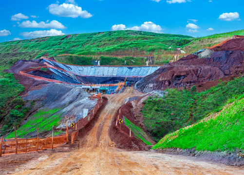 Iron ore extraction infrastructure in Minas Gerais, Brazil. Open-pit mining site showing rich red earth, dirt access roads, and construction amidst green hills.