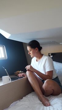 Young woman using a laptop and drinking coffee while working inside a comfortable sailing yacht cabin. Digital nomad lifestyle, remote work, freedom, travel and living aboard a sailboat.