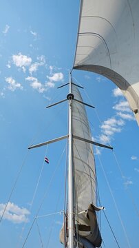 Curved white sail towering above a sailing yacht under a blue sky. Wind powered sailing and freedom on the open sea.
