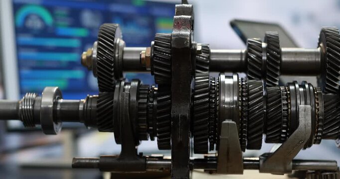 Close-up of a manual transmission gearbox with metal gears, shafts and bearings in a workshop setting.