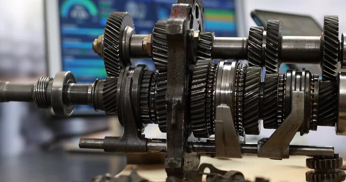 Close-up of a manual transmission gearbox with metal shafts, gears and bearings in an automotive repair workshop.