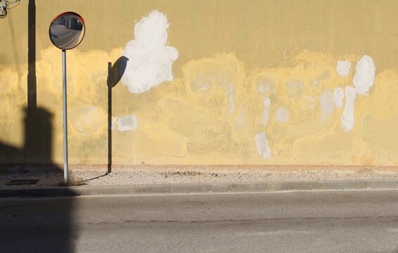 Peeled and stained plaster wall with road convex mirror on the left. Gravel sidewalk and street in front. Grunge background for copy space. Add text.