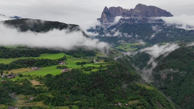 Rugged mountain cliffs tower over forested valleys and hillside meadows in Dolomites, South Tyrol, Italy. Drone footage