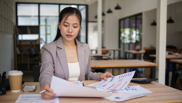 Asian businesswoman comparing multiple financial reports for business planning.