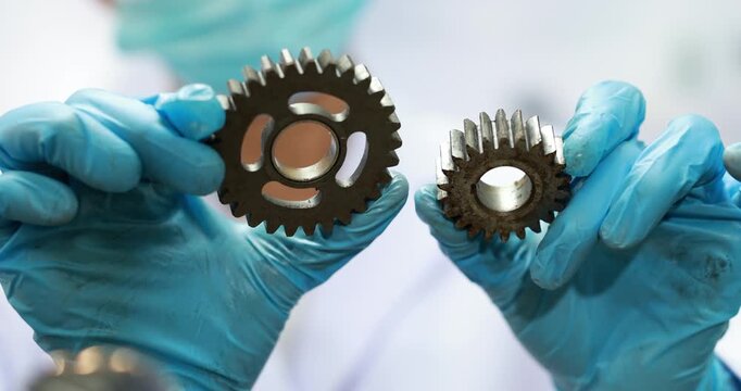 Close-up of blue gloved hands holding two metal gears, machine maintenance, engineering work and industrial repair.