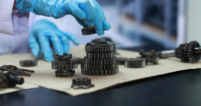 Technician in blue protective gloves assembling metal gears on a workbench in a clean industrial workshop.