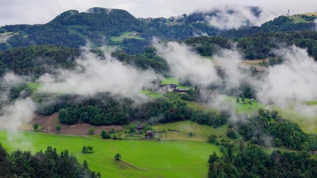 Farmhouses dot green hills as low clouds settle over rural landscape in Dolomites. Mountain countryside in Dolomites.