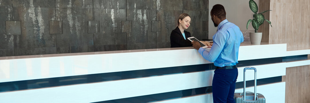 Business traveler checks a tablet with female agent at airport counter with attentive focus. Digital check-in, customer support and corporate travel concept.