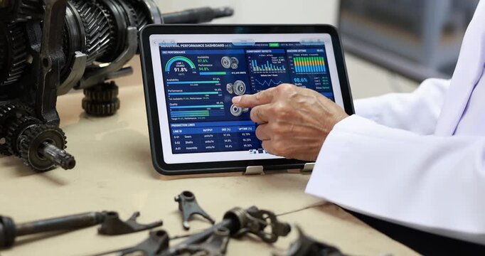Technician in a white lab coat uses a tablet with data charts beside industrial gears and hand tools on a workshop bench.