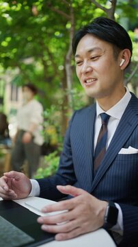 Businessman talking in an online meeting with wireless earphones outdoors