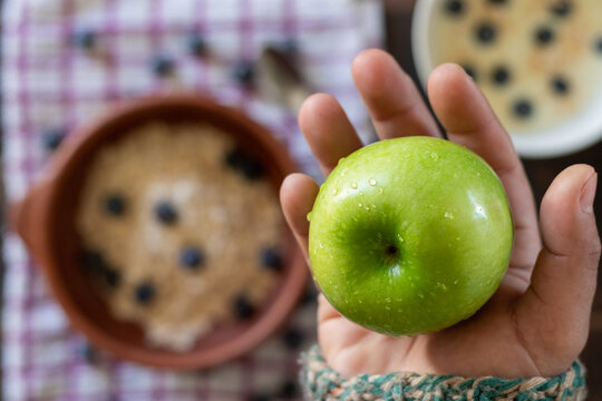 Aerial view of a hand holding a beautiful, fresh, newly washed green apple high in the air against a background of healthy food
